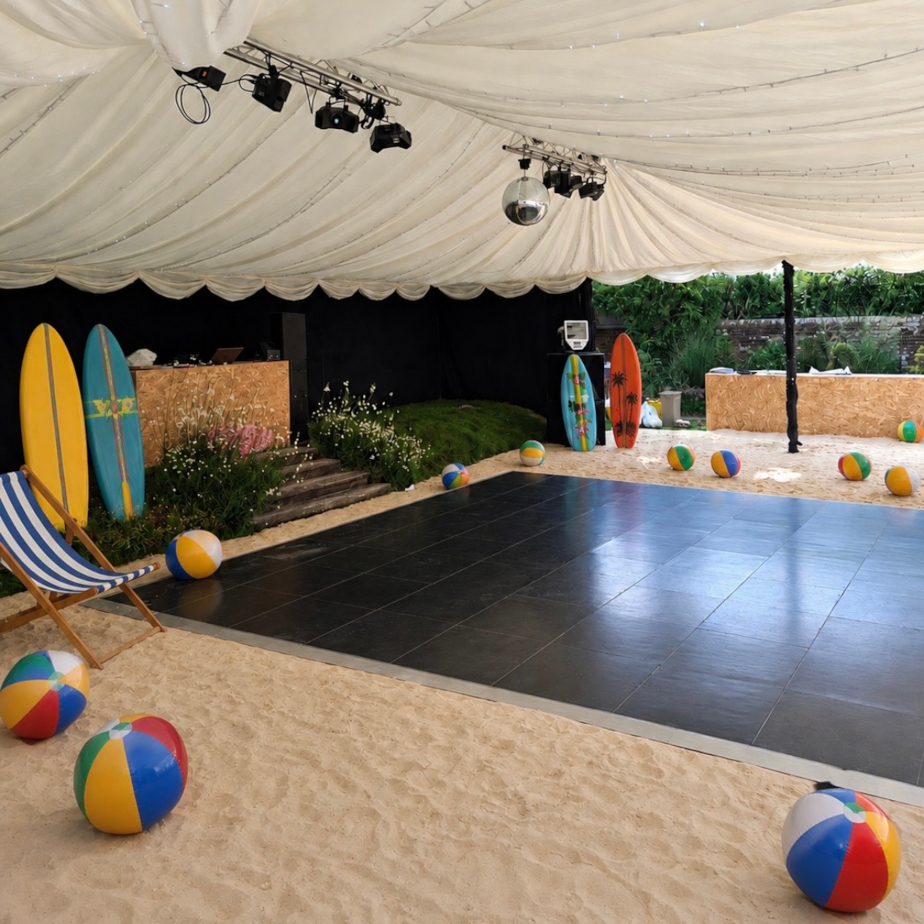 Marquee interior styled as a glamorous beach venue with real sand, dance floor, and beach props